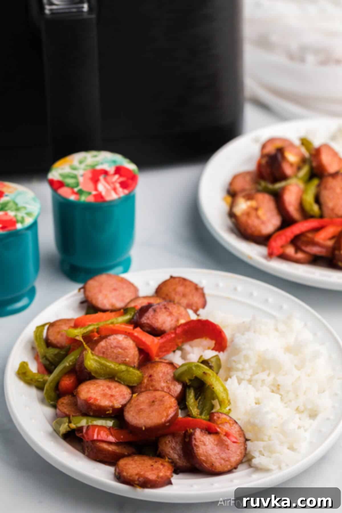 Crispy Air Fryer Sausage and Peppers 8 air fryer sausage and peppers on a white plate with a side of rice.