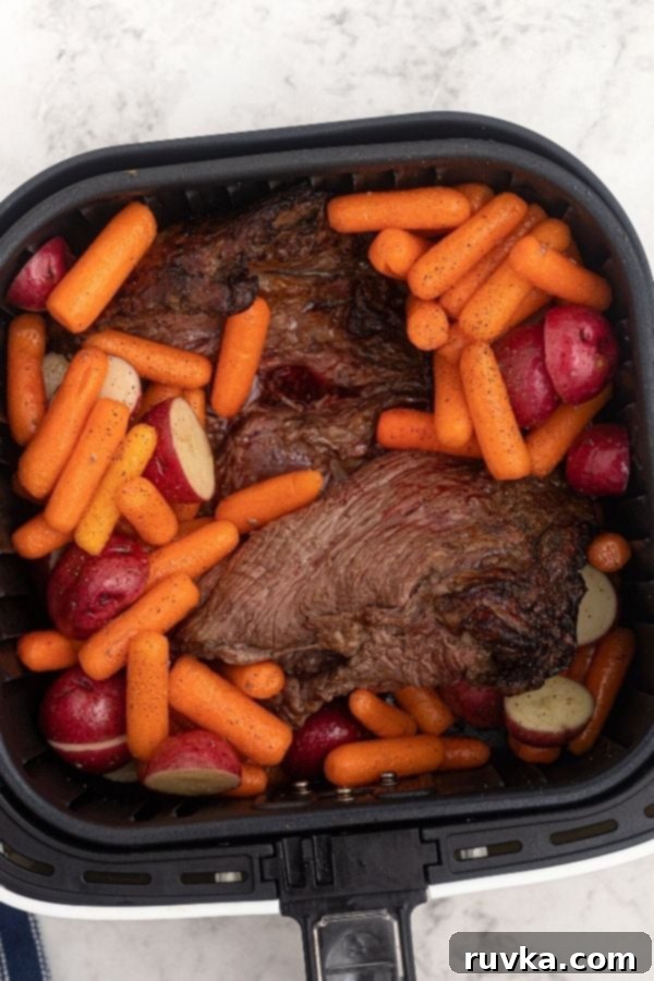 Crispy Air Fryer Top Round 4 Roast in the air fryer basket, cooking with potatoes and carrots.