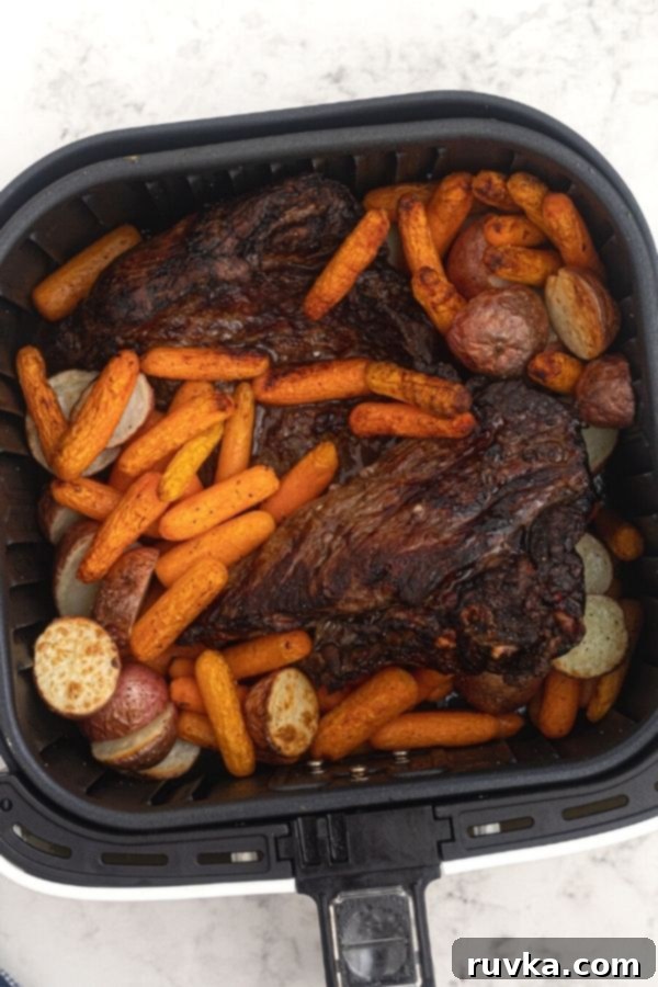 Crispy Air Fryer Top Round 5 Roast, cooked in the air fryer basket, surrounded by potatoes and carrots.