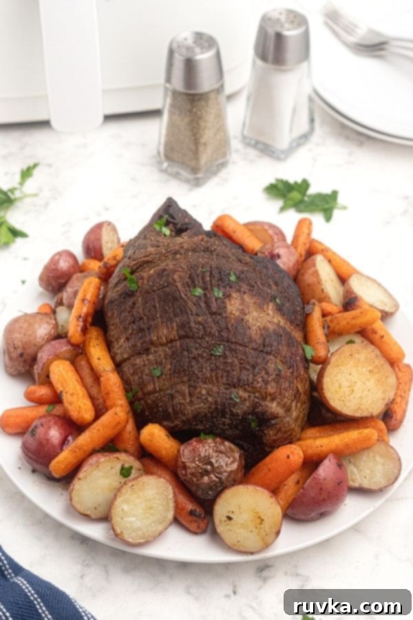 Crispy Air Fryer Top Round 6 Juicy Top Round Roast served on a white plate, with potatoes, and carrots, seasoned with salt and pepper.