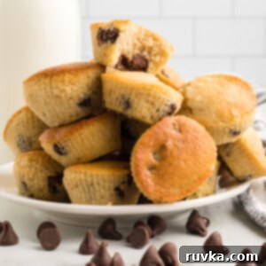 Easy Air Fryer Chocolate Chip Muffins 11 A round white plate beautifully stacked with golden-brown chocolate chip air fryer muffins, perfectly baked and inviting. Scattered chocolate chips are sprinkled around on the table in front of the plate, adding a touch of delicious chaos.