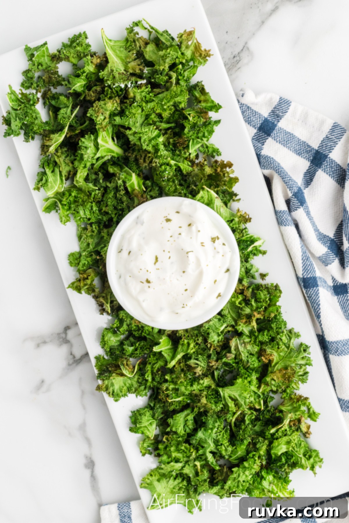 Crispy Air Fryer Kale Chips 8 Air fryer kale chips fully cooked and served on a white rectangle serving tray with a white bowl of greek yogurt in the center.