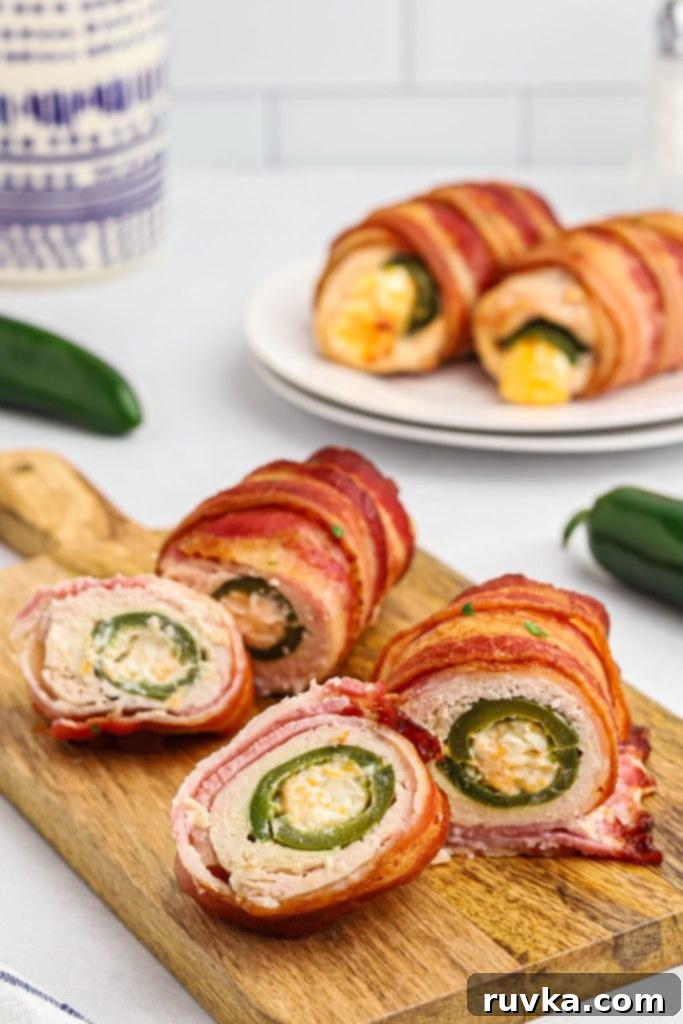 Crispy Air Fryer Chicken Jalapeno Poppers 2 Crispy bacon wrapped around chicken and jalapenos stuffed with cheese on a wooden cutting board.