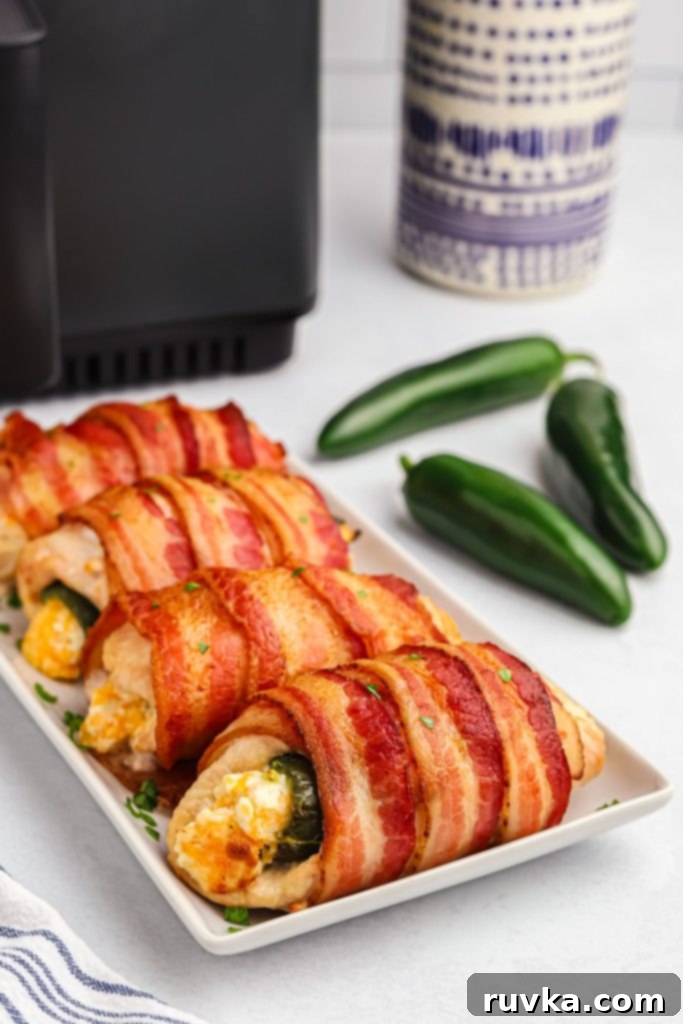 Crispy Air Fryer Chicken Jalapeno Poppers 11 Crispy bacon-wrapped chicken breast featuring a visible jalapeno popper center, served on a white rectangular plate.