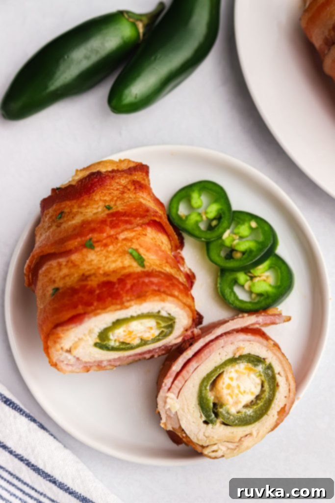 Crispy Air Fryer Chicken Jalapeno Poppers 12 A perfectly cooked Air Fryer Chicken Jalapeno Popper, sliced in half to reveal its creamy cheese and jalapeno filling, wrapped in chicken and crispy bacon, served on a small white plate.