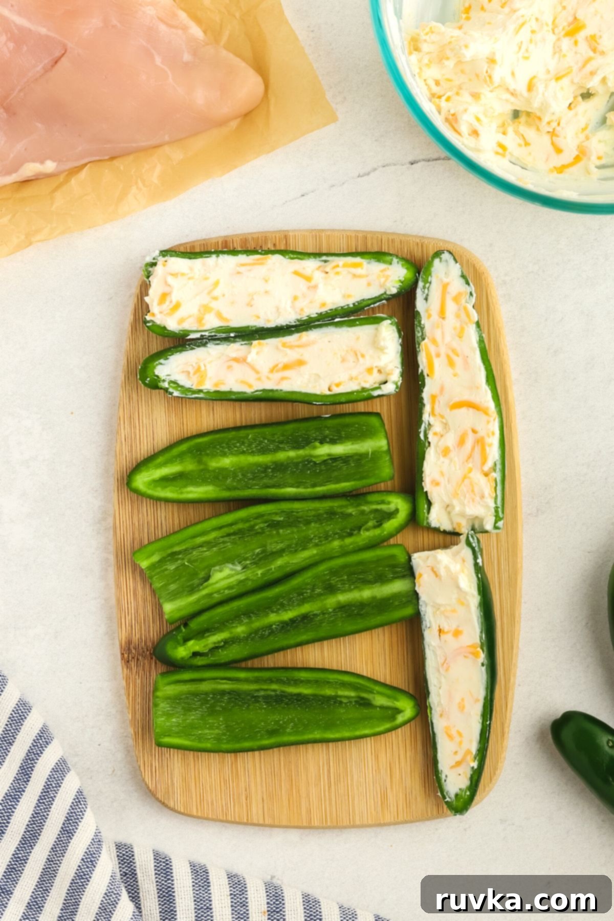 Crispy Air Fryer Chicken Jalapeno Poppers 5 Jalapeno halves filled with a creamy cheese mixture and pressed back together on a cutting board.