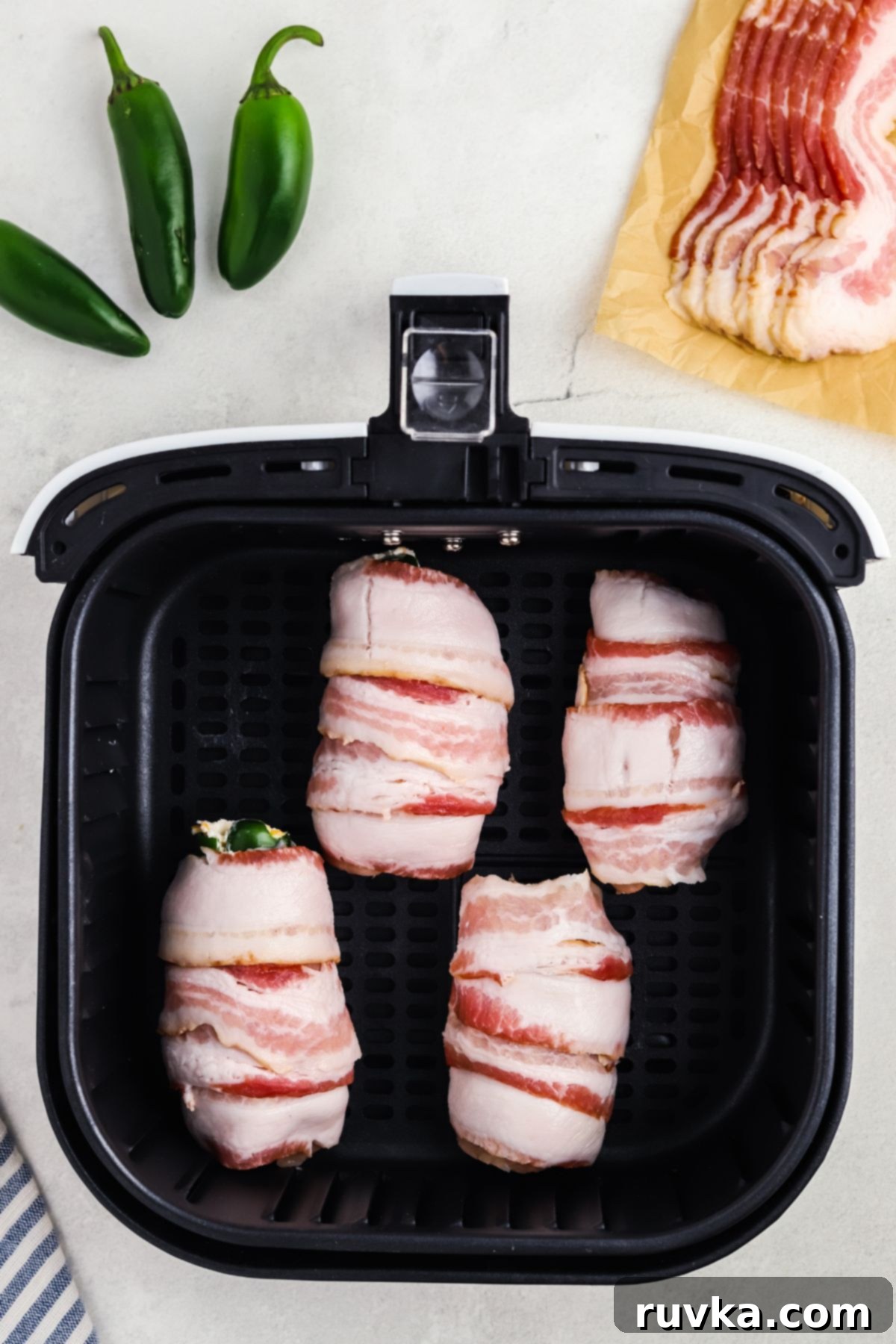 Crispy Air Fryer Chicken Jalapeno Poppers 8 Bacon-wrapped chicken and jalapeno poppers arranged in an air fryer basket, ready for cooking.