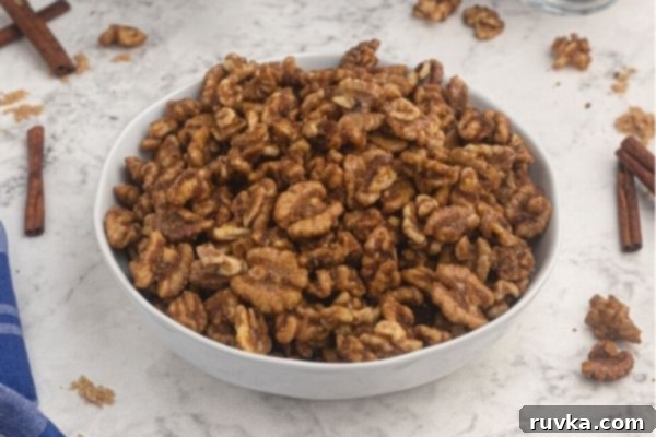 Crispy Sweet Air Fryer Walnuts 2 Candied walnuts served in a white bowl with cinnamon sticks and walnuts scattered on a white marble counter.