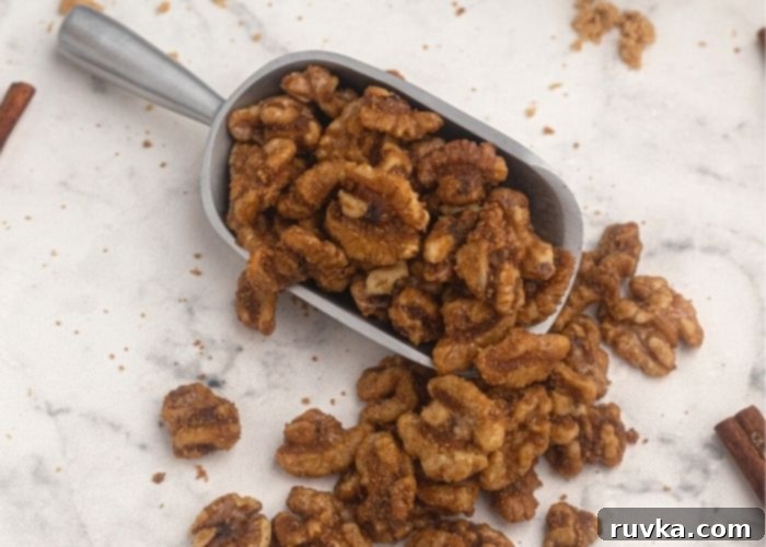 Crispy Sweet Air Fryer Walnuts 3 Candied walnuts served in silver scoop with cinnamon sticks and walnuts scattered on a white marble counter.