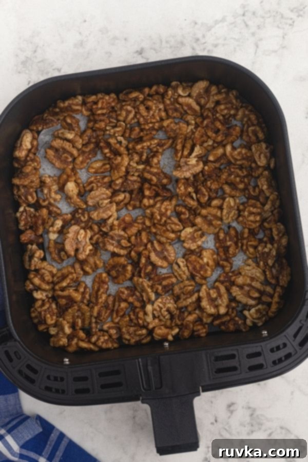 Crispy Sweet Air Fryer Walnuts 4 Uncooked walnuts in an air fryer basket, seasoned with melted butter, sugars, and the other ingredients.