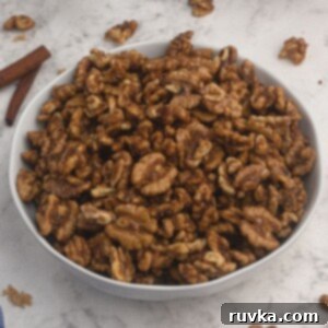 Crispy Sweet Air Fryer Walnuts 6 Candied Walnuts, served in a white bowl with cinnamon sticks and scattered walnuts on the table