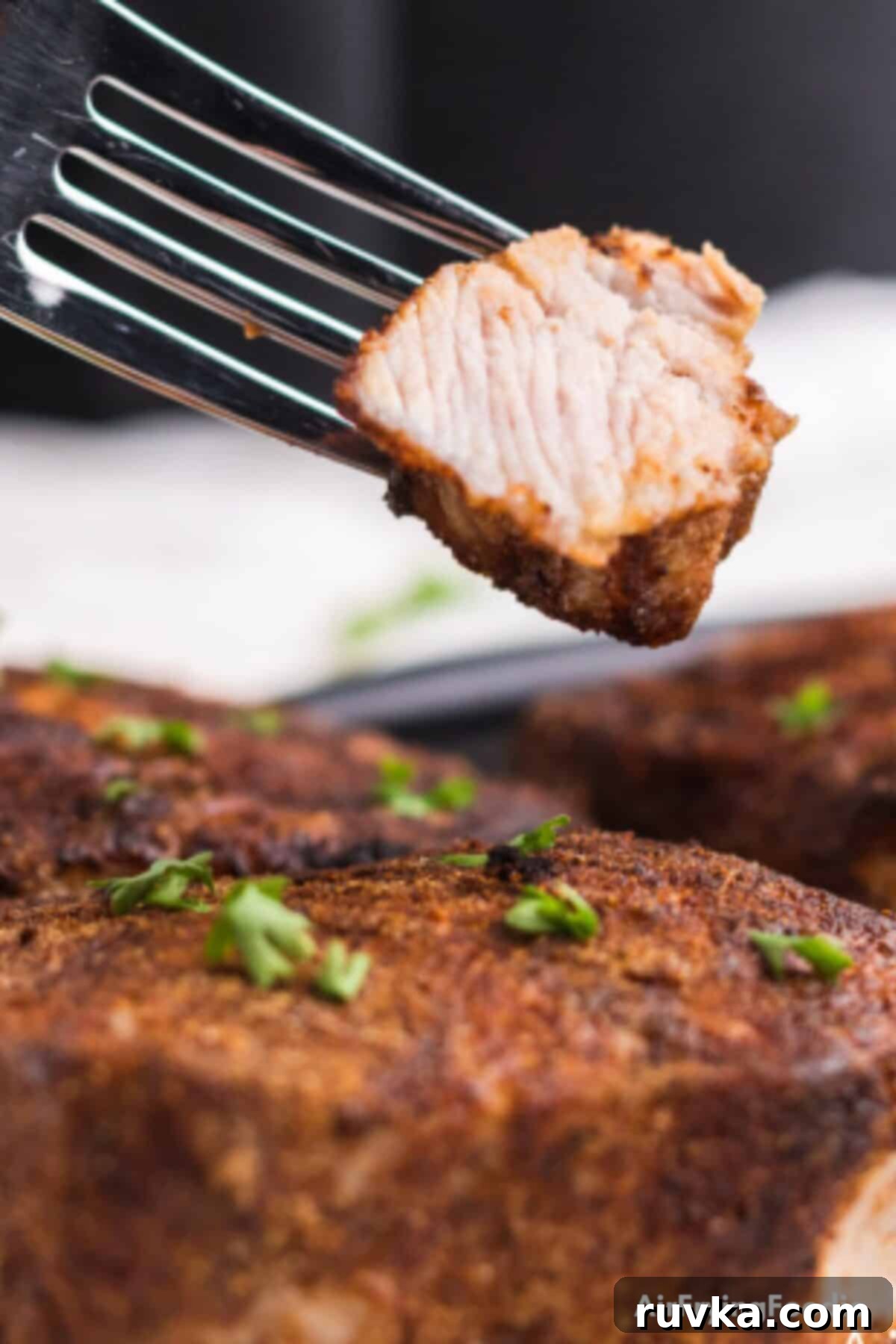 Juicy Air Fryer Pork Chops 2 Close up of seasoned air fryer pork chops, with a bite on a fork, ready to eat. The chops are golden brown and look incredibly juicy.