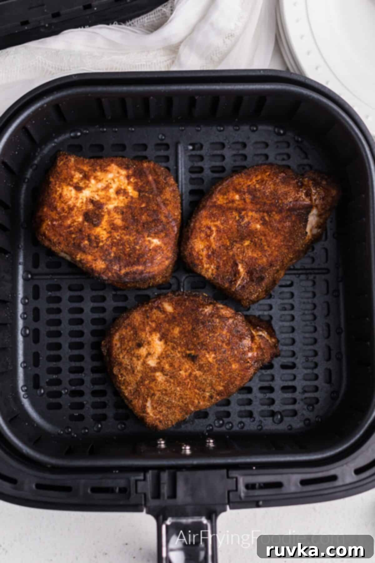 Juicy Air Fryer Pork Chops 5 Pork chops in the basket of the air fryer, fully cooked and ready to serve. They look golden and succulent.