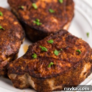 Juicy Air Fryer Pork Chops 6 Pork chops on a white plate and topped with fresh parsley for garnish.