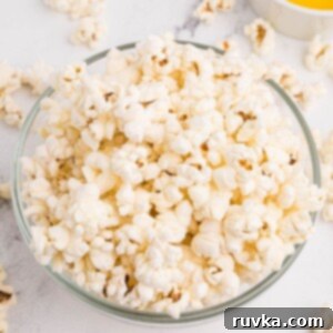 Air-Popped Perfection 9 Clear glass bowl filled with fluffy popcorn and a small bowl of melted butter on a marble table.