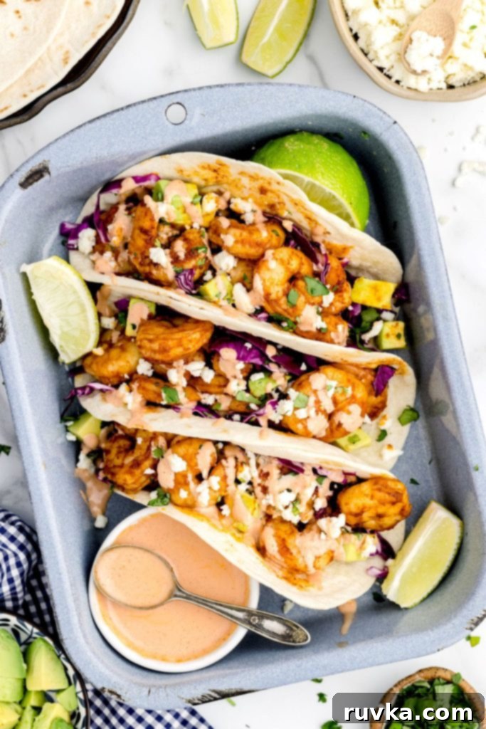 Crispy Air Fryer Shrimp Tacos 2 Golden seasoned shrimp in tortillas and stacked in a pan with cut lime wedges and toppings, ready to be served.