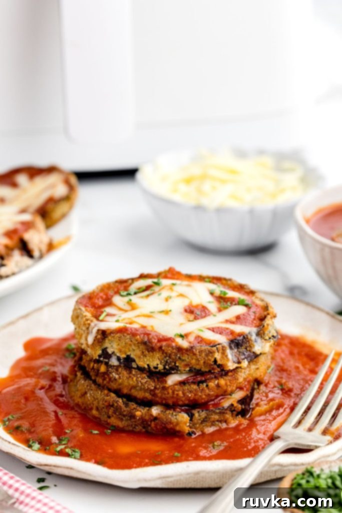 Air Fried Eggplant Parmesan 2 Crispy golden parmesan covered eggplant slices on a white plate in front of the air fryer.