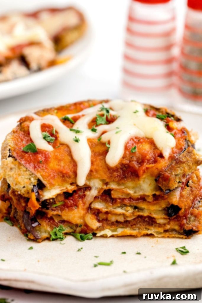 Air Fried Eggplant Parmesan 11 Crispy eggplant parmesan stacked on a white plate covered in marinara sauce and melted mozzarella cheese