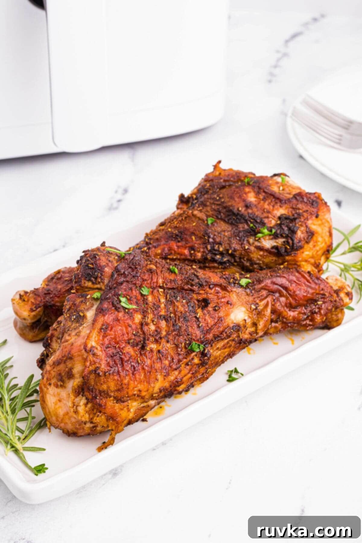 Crispy Air Fryer Turkey Legs 2 Crispy turkey legs on a white rectangle plate seasoned with parsley flakes in front of the air fryer.