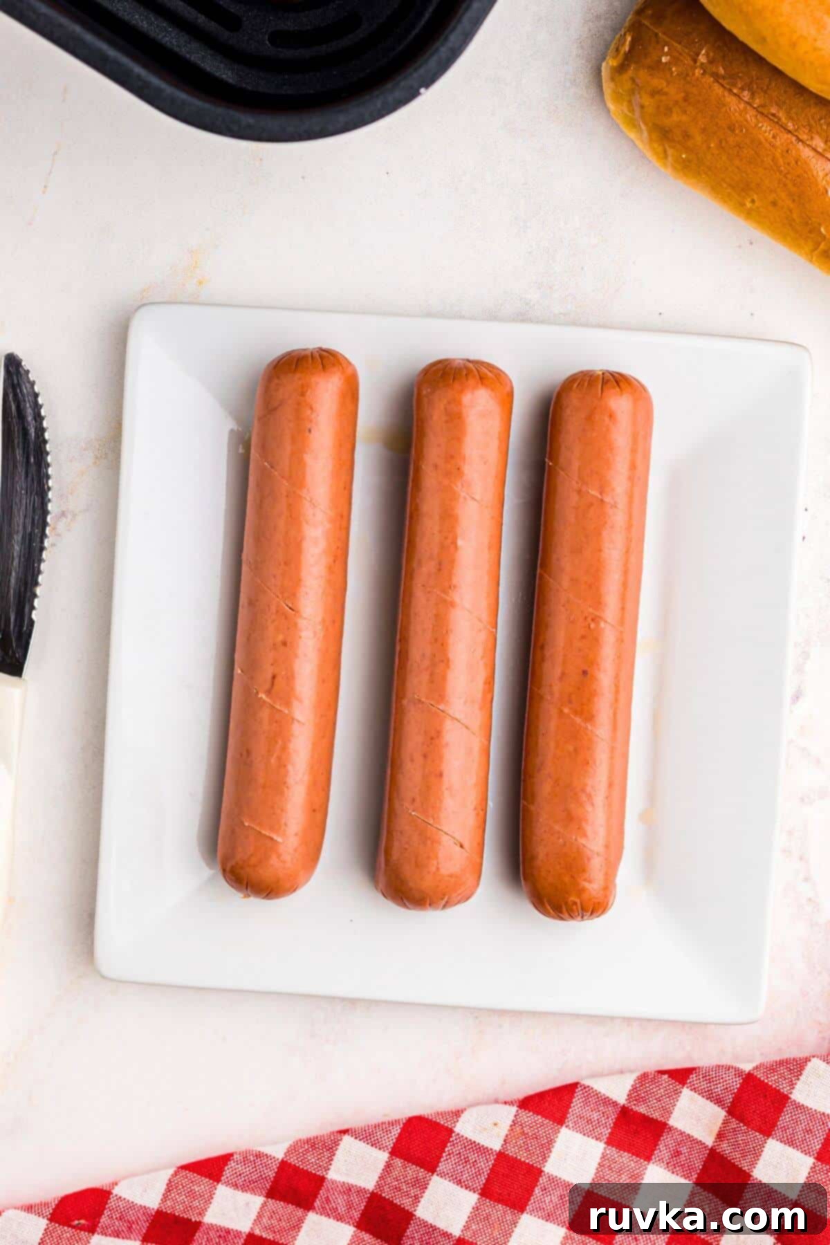 Air Fryer Hot Dog Hack 4 Juicy franks with slits cut into them on a white plate.