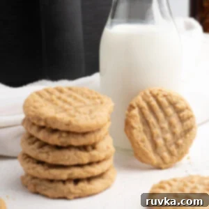 Easy Air Fryer Christmas Cookies 13 A stack of golden peanut butter cookies made in the Air Fryer, with a glass of milk and the Air Fryer in the background, ready for a delicious snack.
