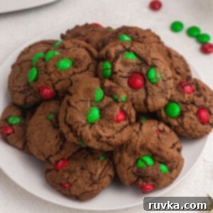 Easy Air Fryer Christmas Cookies 4 Freshly baked chocolate brownie cookies with festive red and green M&M's baked in, served on a white plate.