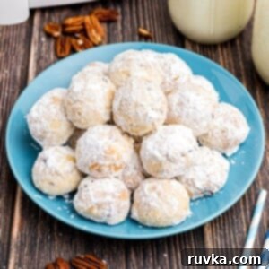 Easy Air Fryer Christmas Cookies 6 White powdered sugar coated snowball cookies stacked on a blue plate, perfect for a winter treat.