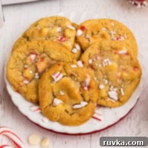 Easy Air Fryer Christmas Cookies 9 Golden cookies on a white plate with peppermints and white chocolate chips scattered on the table, creating a festive scene.