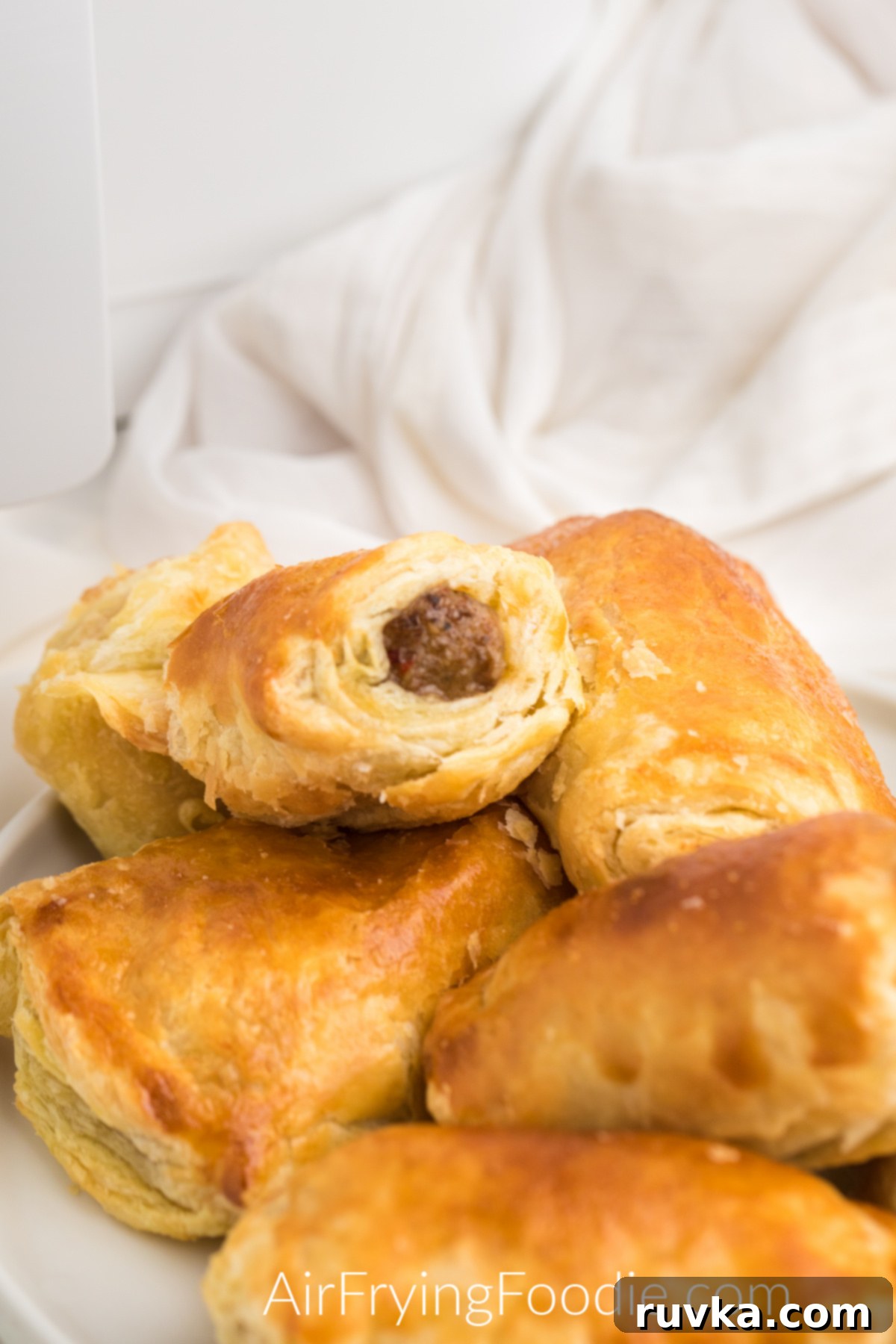 Perfect Air Fryer Sausage Rolls 2 Flaky sausage rolls made in the air fryer, served on a platter. Golden brown puff pastry encasing savory sausage, ready to be enjoyed.