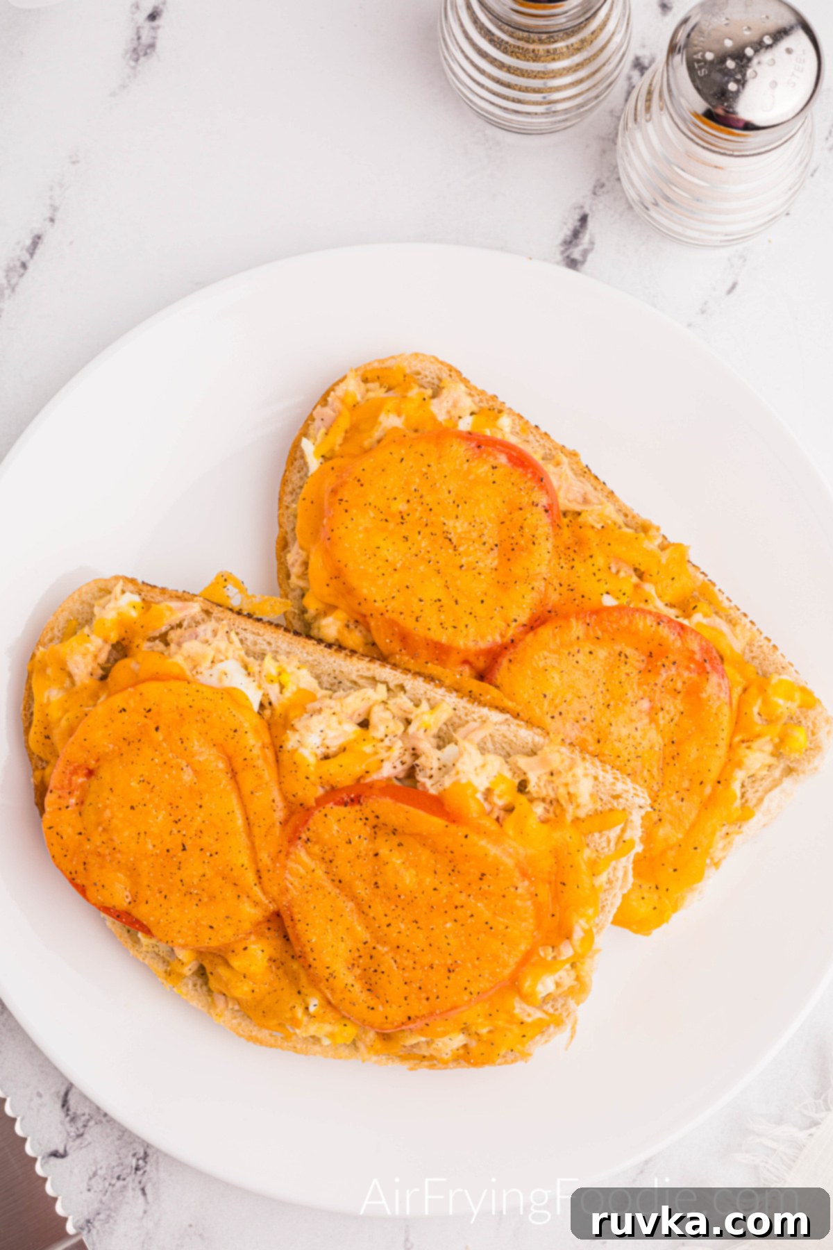 Crispy Air Fryer Tuna Melt 11 Overhead shot of a tuna melt cooked In the air fryer, topped with tomatoes and melted cheese, and served on a round white plate.