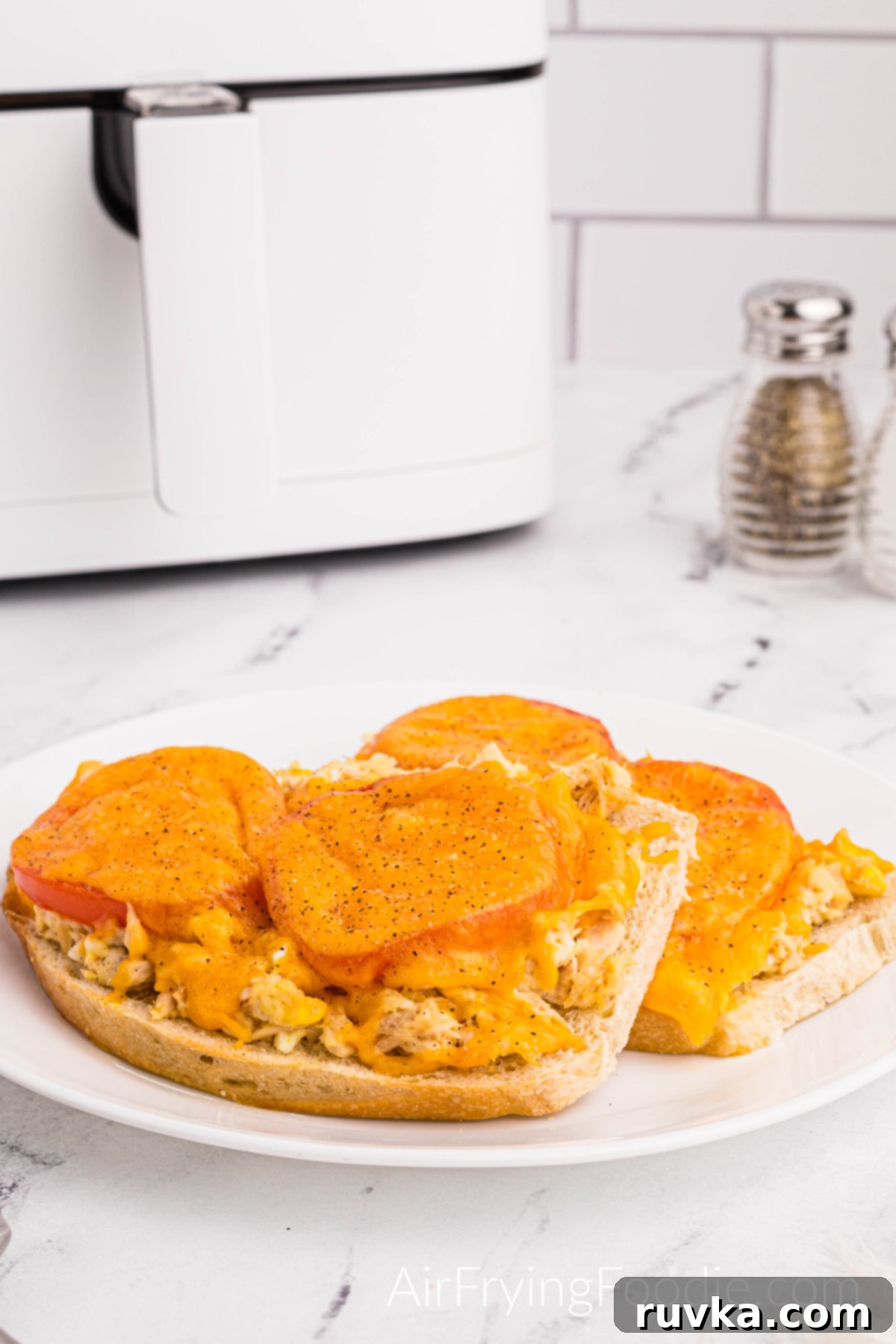 Crispy Air Fryer Tuna Melt 12 A tuna melt cooked In the air fryer, topped with tomatoes and melted cheese, and served on a round white plate. There is a salt and pepper shaker at the top right of the picture, and the base of the air fryer is to the right.