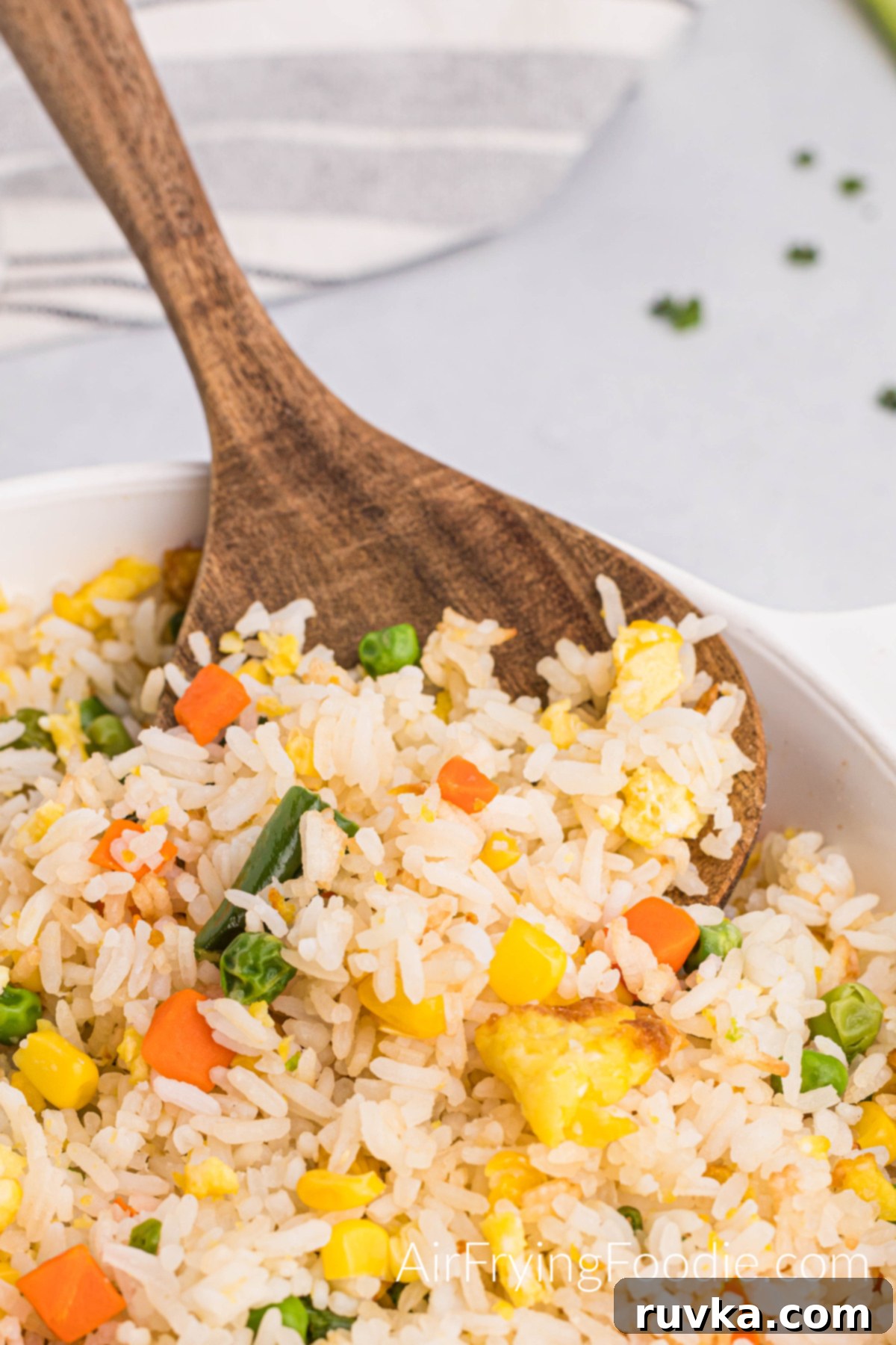 Quick Air Fryer Fried Rice 11 A close-up view of fluffy, perfectly cooked air fryer fried rice, scooped onto a wooden spoon, highlighting the separated grains, vibrant vegetables, and tender scrambled eggs.