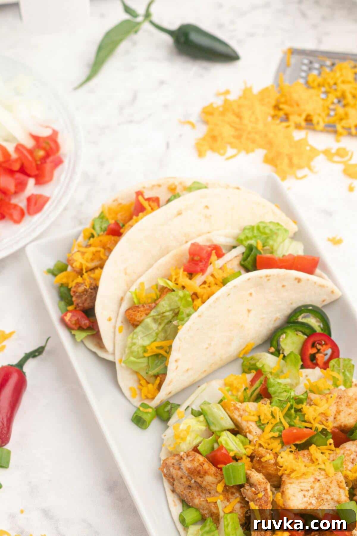Crispy Air Fryer Chicken Street Tacos 5 Flour tortillas being filled with seasoned chicken, shredded lettuce and other taco fillings.