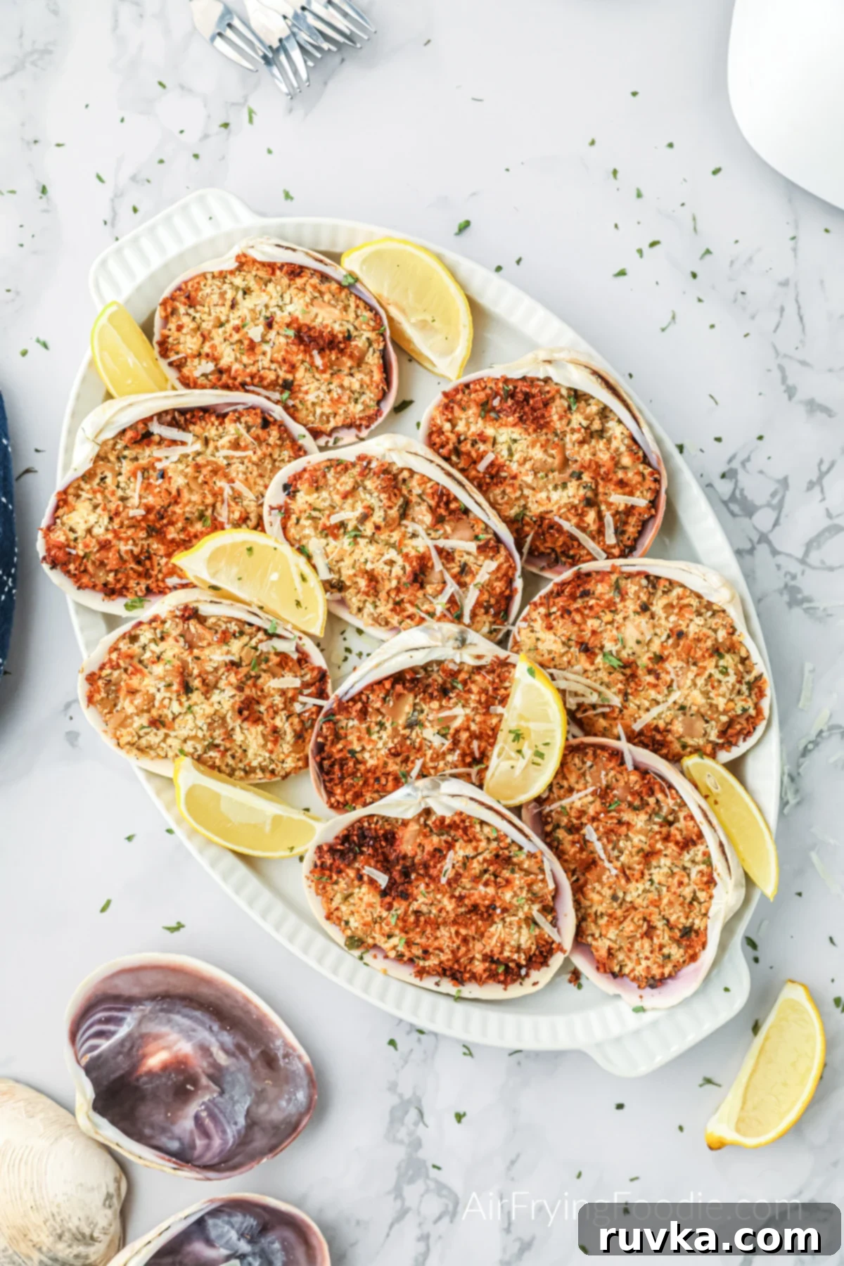 Crispy Air Fryer Stuffed Clams 2 Golden brown air fryer stuffed clams on a white plate with fresh lemon wedges, ready to be served as a gourmet appetizer.