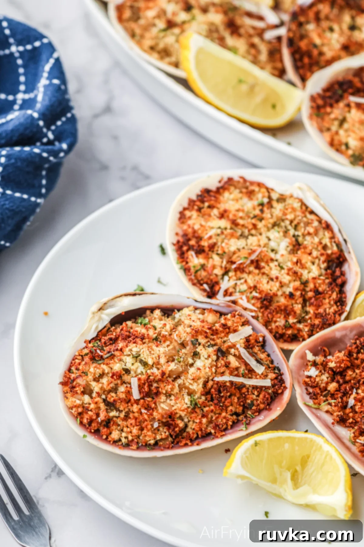 Crispy Air Fryer Stuffed Clams 10 Beautifully arranged air fried stuffed clams on a pristine white serving plate, accompanied by vibrant lemon wedges, highlighting their appetizing appeal and readiness to be served.