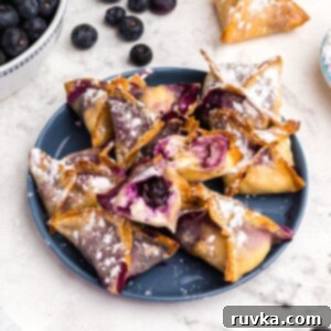 Crispy Air Fryer Blueberry Cheesecake Wontons 11 Crispy golden wontons filled with blueberry cheesecake filling on a blue plate.