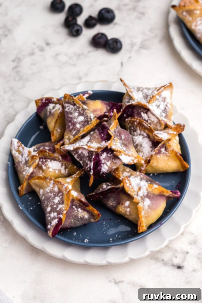 Crispy Air Fryer Blueberry Cheesecake Wontons 10 Crispy wontons stacked on a blue plate sprinkled with powdered sugar.