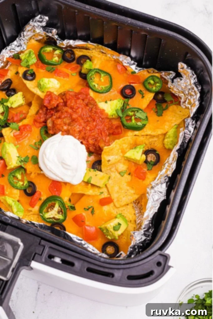 Ultimate Air Fryer Nachos 2 Tortilla chips spread out in an air fryer basket topped with melted cheese and nacho toppings.