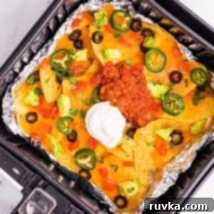 Ultimate Air Fryer Nachos 7 Crispy nachos in an air fryer basket topped with cheese, sour cream and salsa.