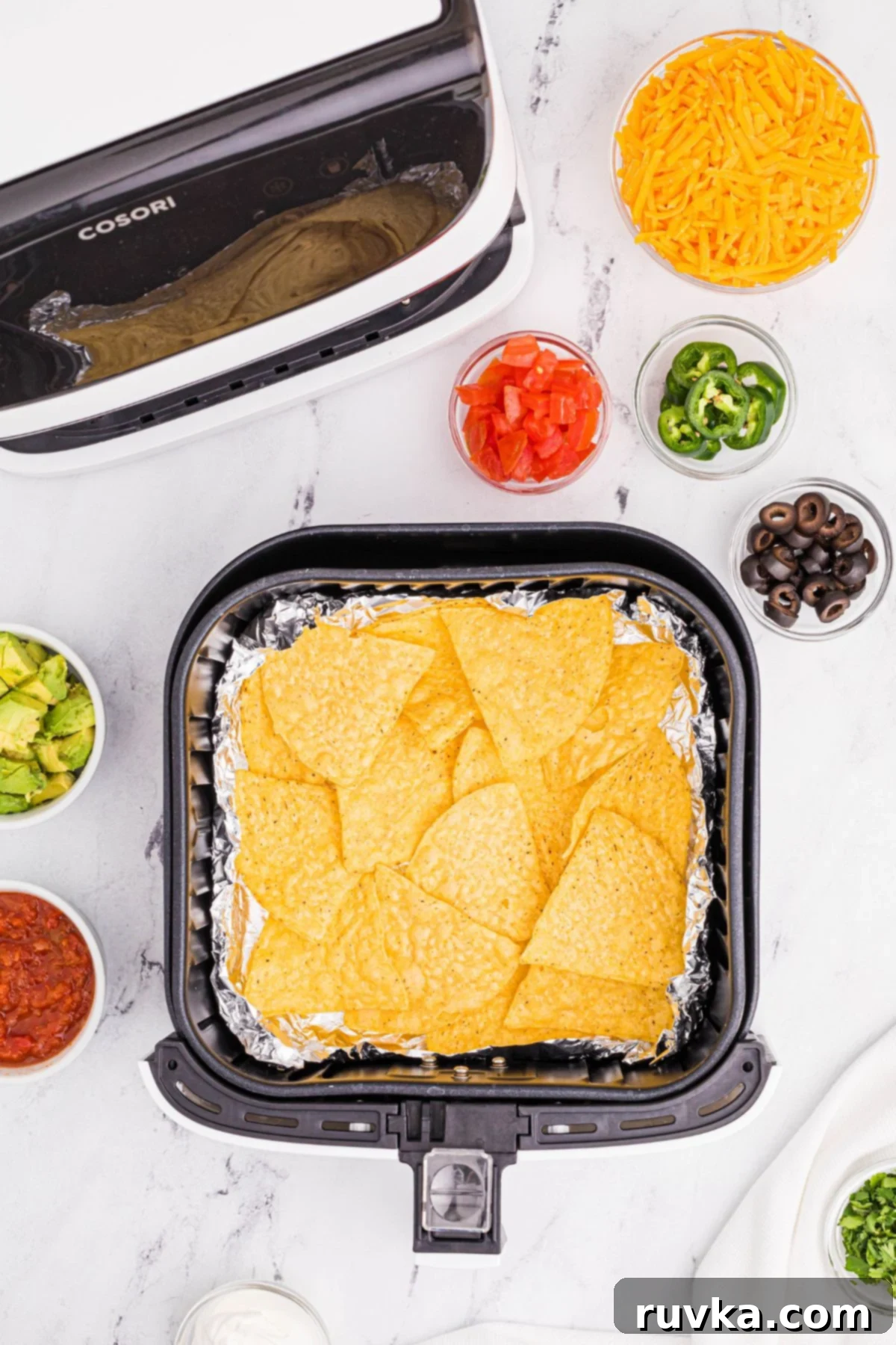 Ultimate Air Fryer Nachos 4 Tortilla chips on a cover of tin foil in the air fryer basket.