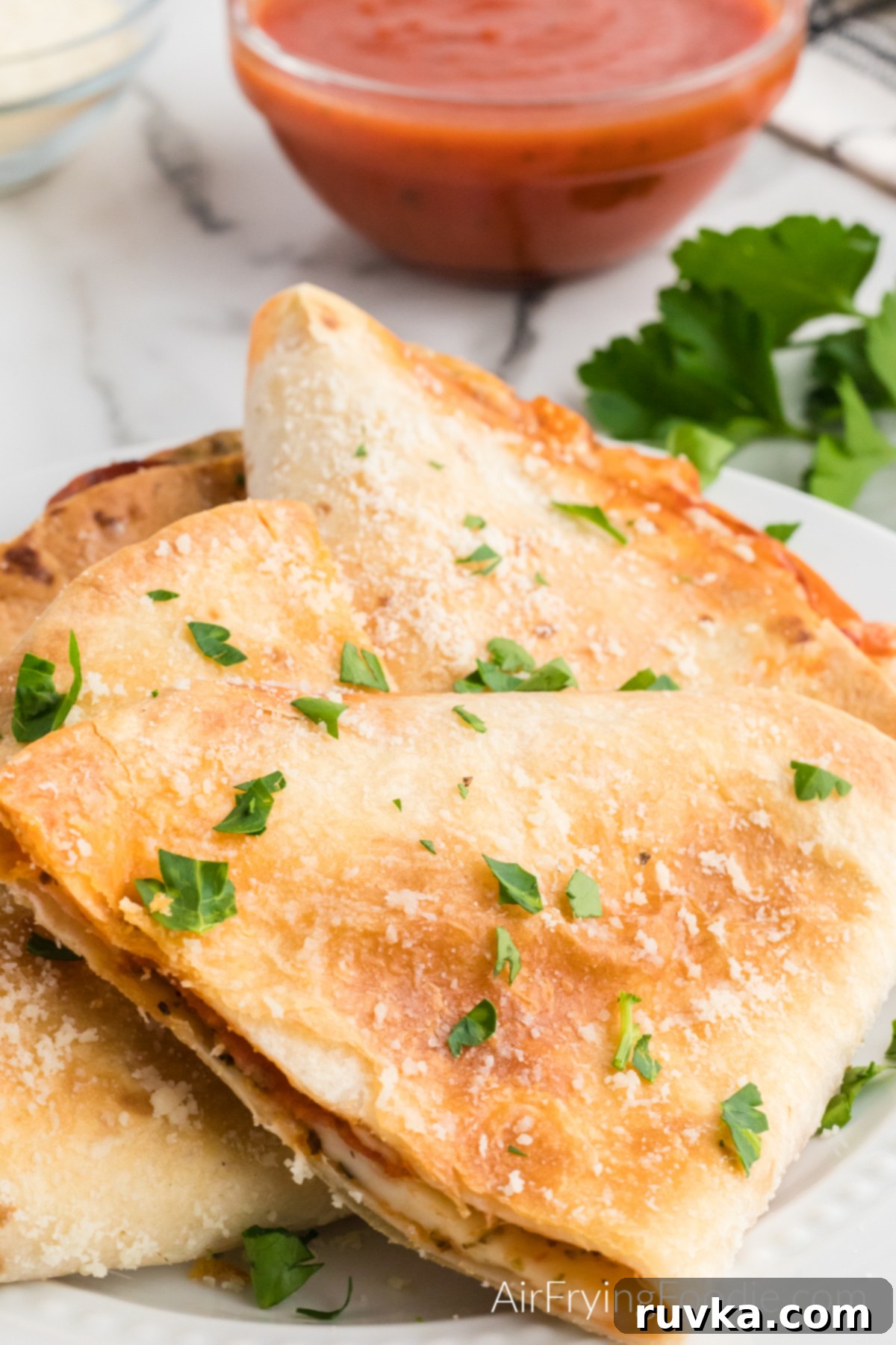 Crispy Air Fryer Pizza Quesadilla 10 Two air fryer pizza quesadillas, garnished with fresh parmesan cheese and parsley, presented on a white plate.