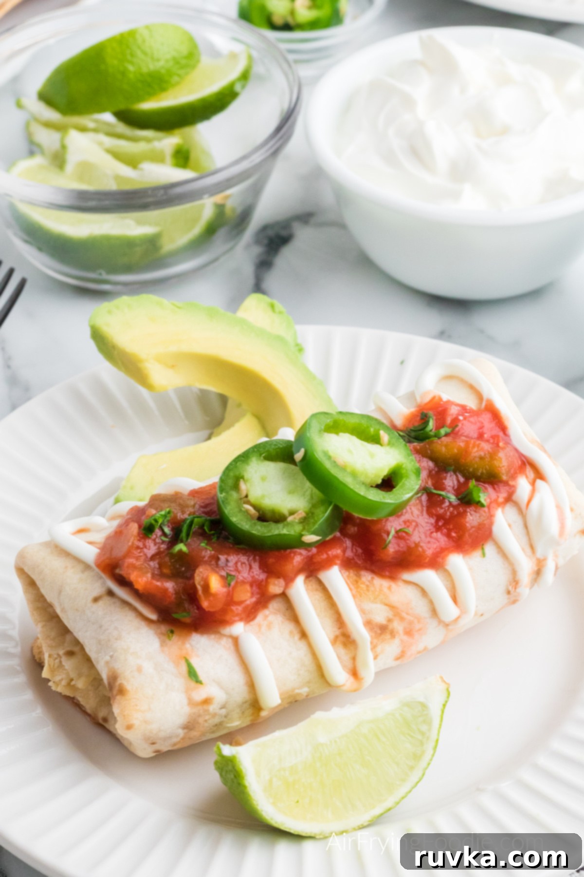 Crispy Air Fryer Chimichangas 2 Crispy Air Fryer Chimichanga topped with sour cream, salsa, and sliced jalapenos on a white plate, ready to be enjoyed.