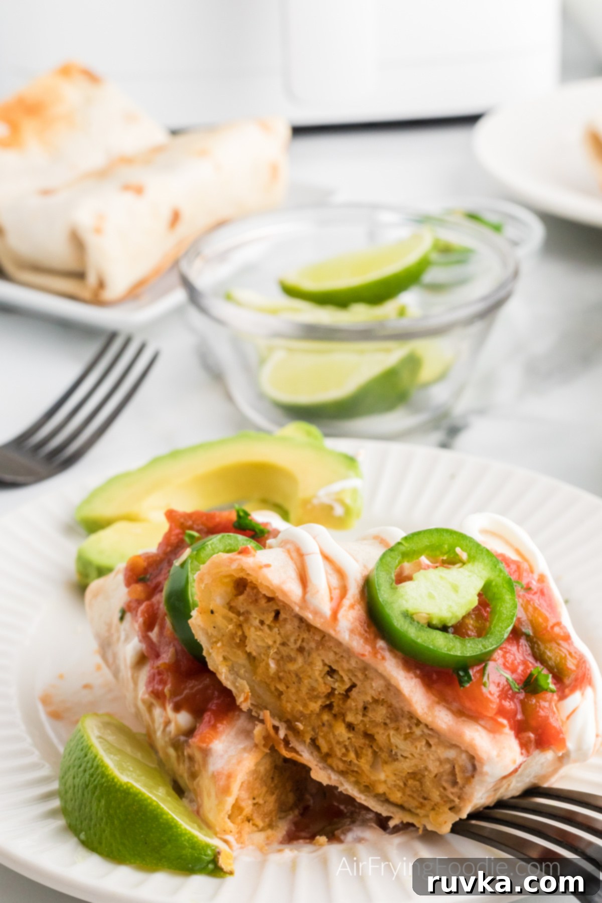 Crispy Air Fryer Chimichangas 9 A perfectly air-fried chimichanga, artfully cut in half to reveal its rich, cheesy chicken filling, adorned with fresh toppings and ready to be savored.