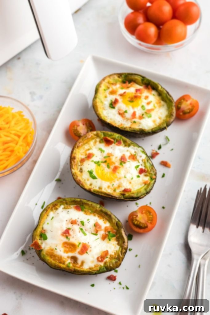 Air Fryer Avocado Egg Boats 2 Juicy avocados filled with fried eggs on a white square plate.