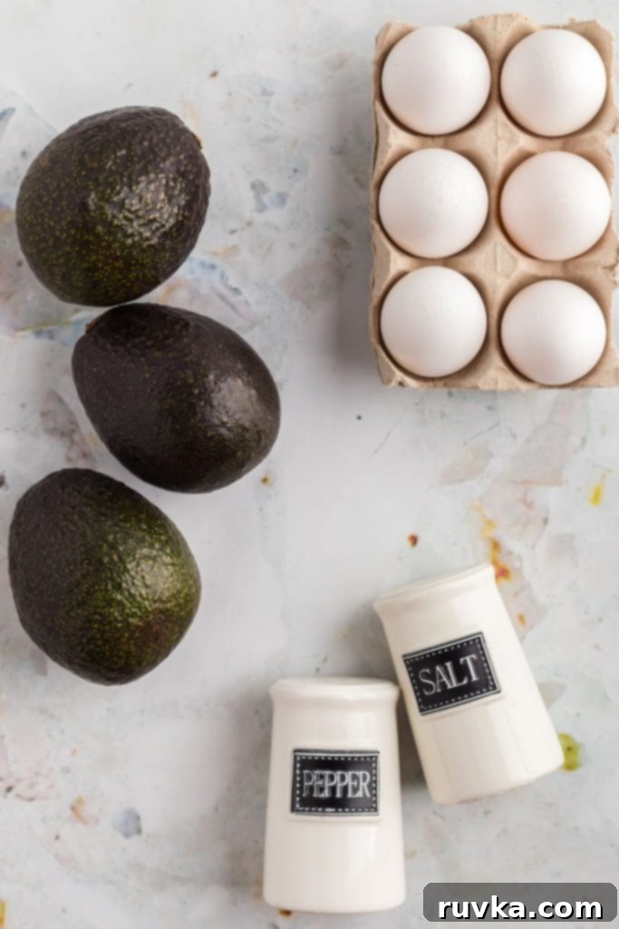 Air Fryer Avocado Egg Boats 3 Ingredients to make avocado eggs on a marble table.