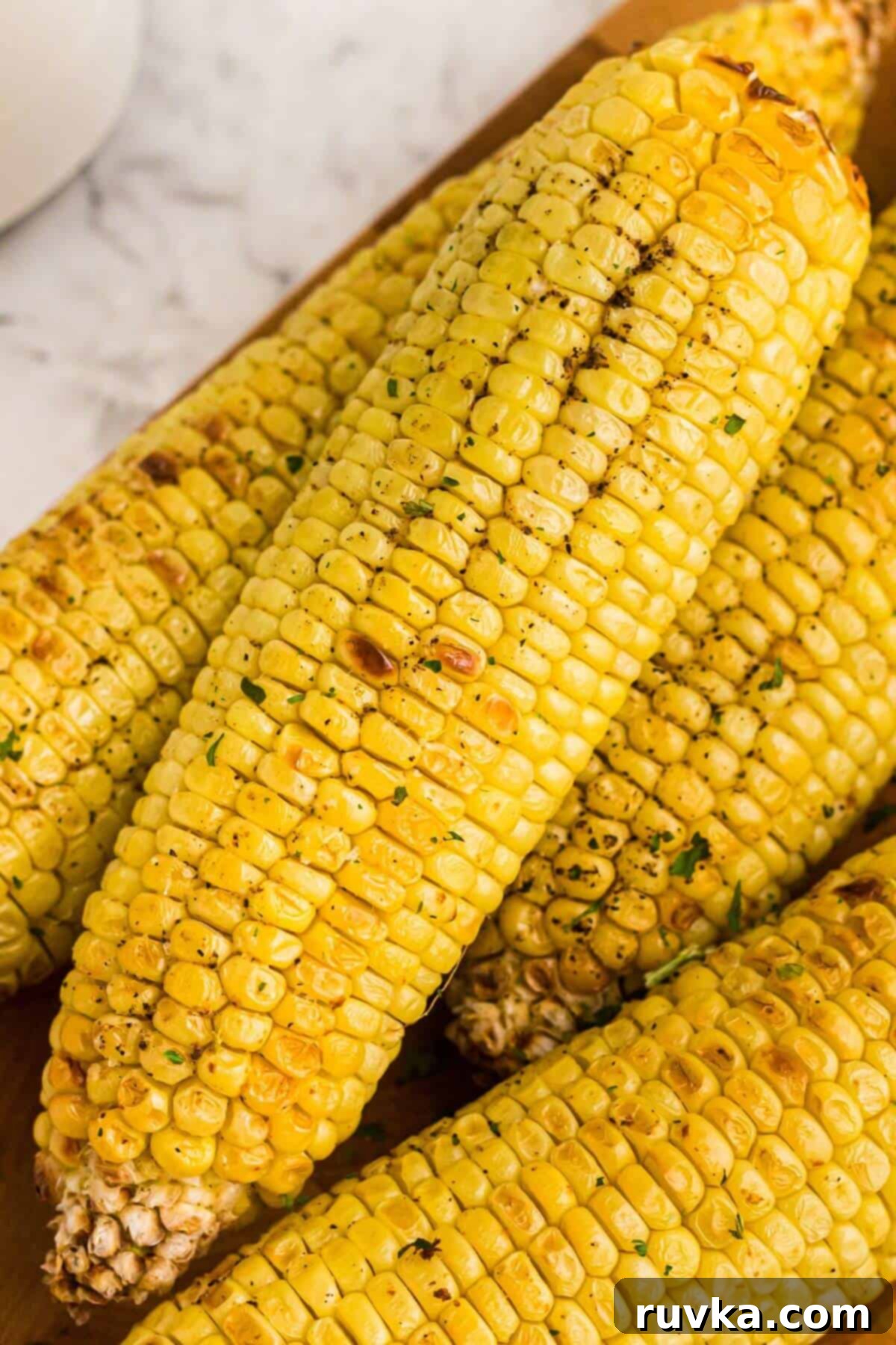 Crispy Air Fryer Corn 2 Golden yellow ears of corn seasoned on a cutting board, ready for the air fryer.