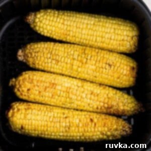 Crispy Air Fryer Corn 7 Golden yellow corn on the cob in the air fryer basket after being cooked and seasoned.