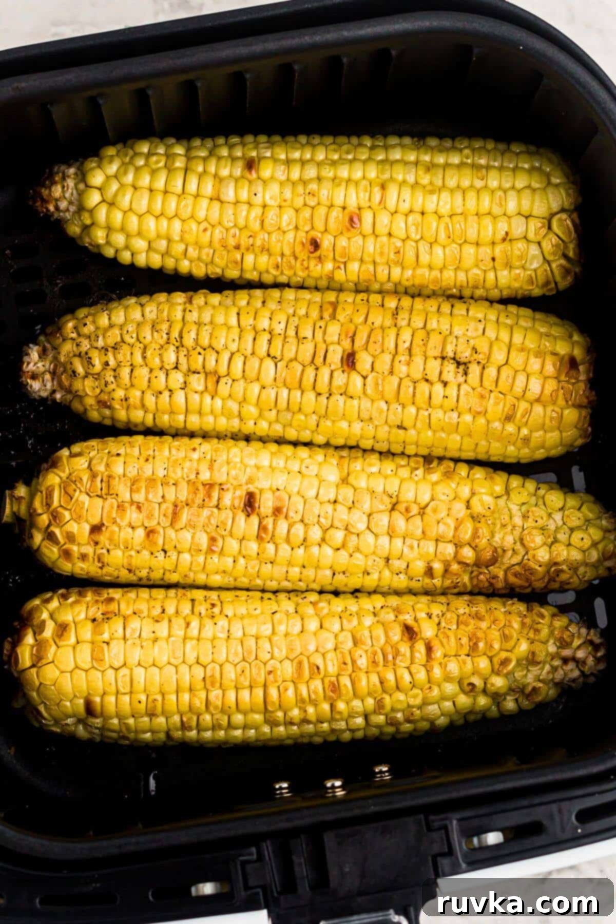 Crispy Air Fryer Corn 5 Golden yellow cooked ears of corn in the air fryer basket, perfectly roasted and ready to serve.