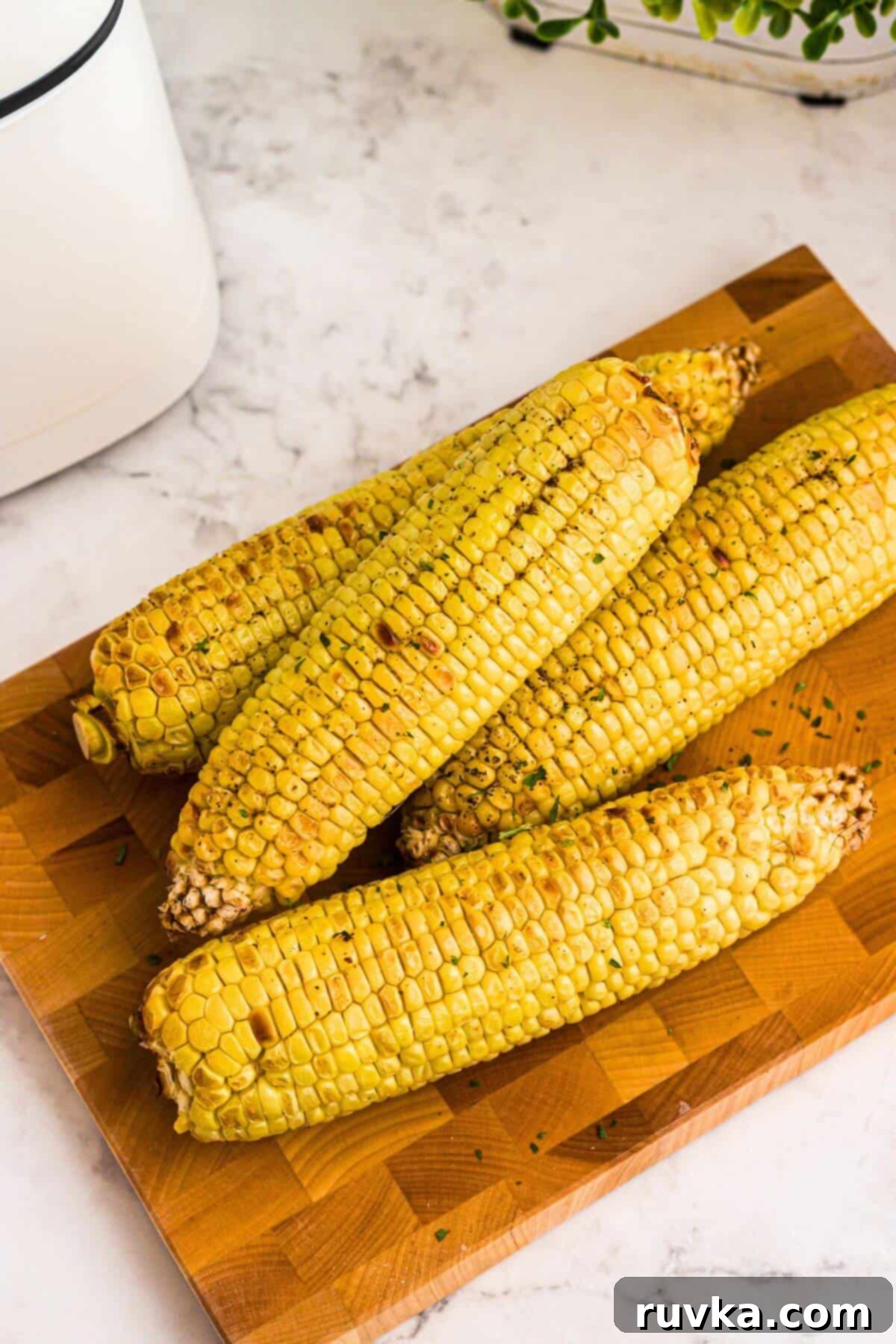 Crispy Air Fryer Corn 6 Golden yellow ears of corn on a wooden cutting board, garnished and ready for serving after air frying.