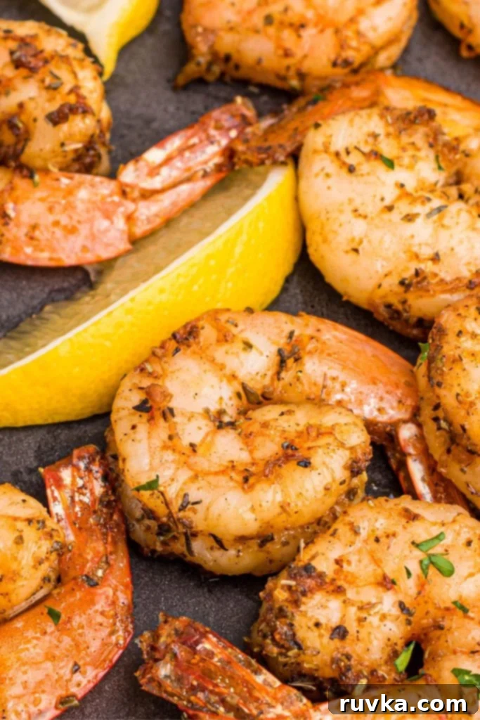 Crispy Air Fryer Shrimp 2 Juicy seasoned shrimp on a dark plate with lemon wedges.